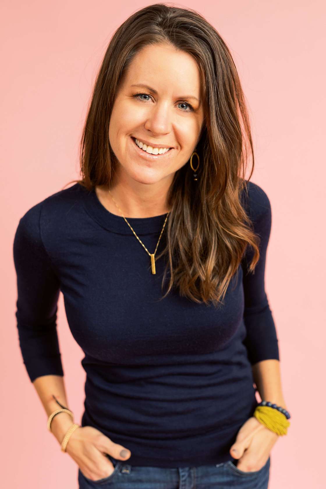 Stacy Barrett, smiling, navy sweater, coral background